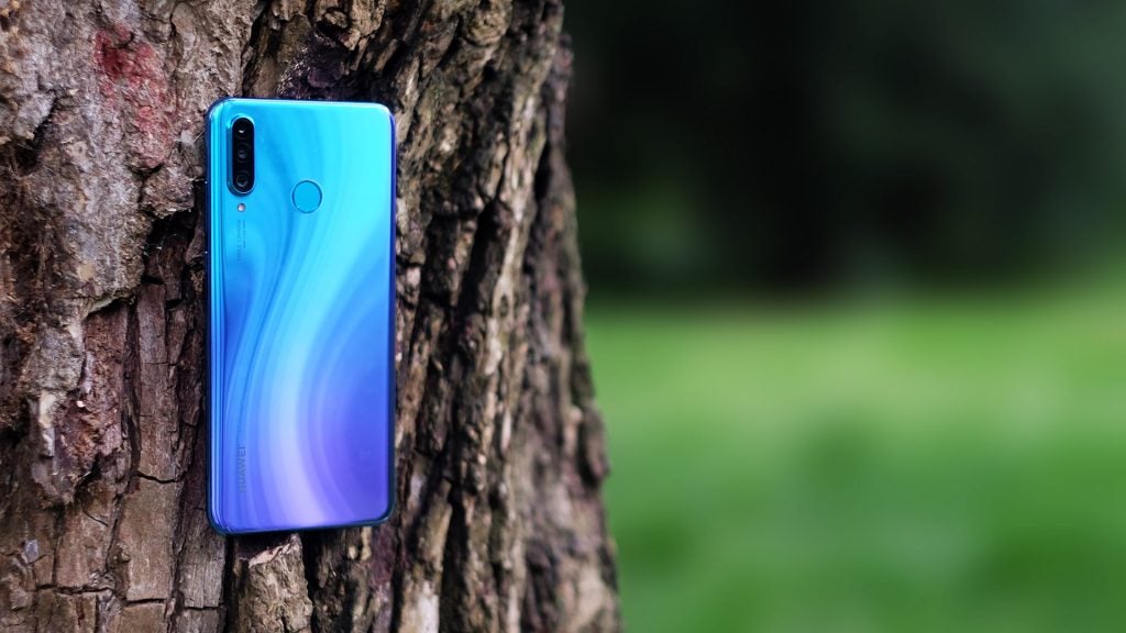 Back panel view of a blue Huawei P30 Lite standing on a tree trunk facing backA Huawei P30 Lite held in hand horizontally displaying picture through camera