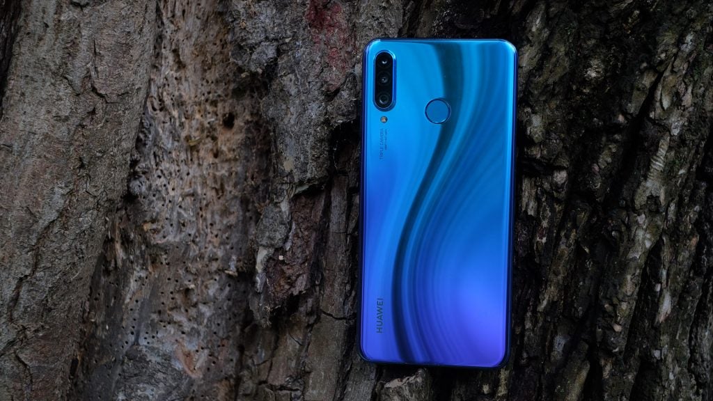 Back panel view of a blue Huawei P30 Lite standing on a tree trunk facing backClose up view of back camera section of a blue Huawei P30 Lite kept facing down on a wooden surface