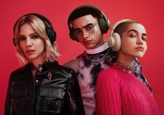 A guy and two girls standing on a red background wearing headphones
