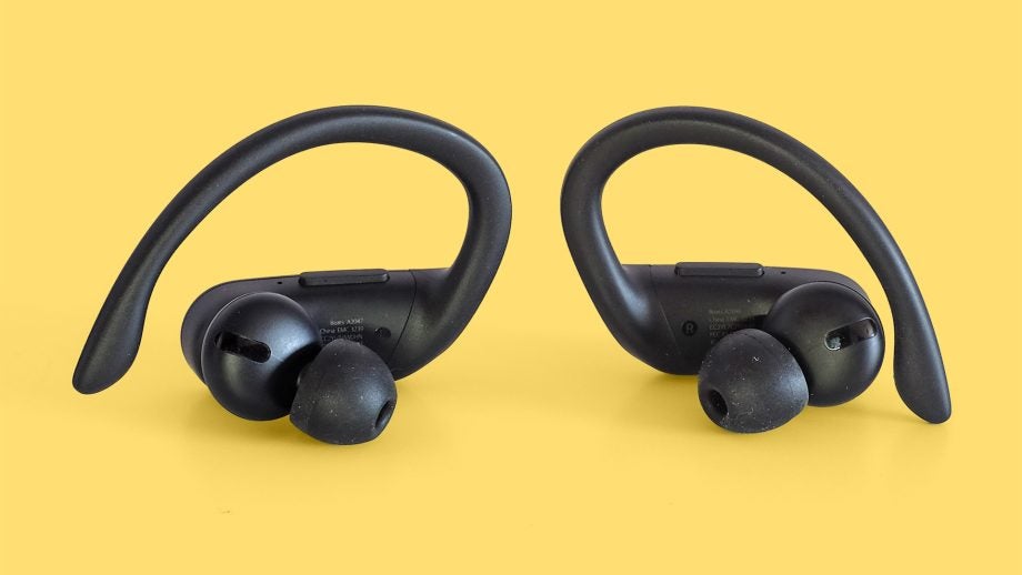 Close up view of a black Powerbeats earbuds kept on a yellow background, front panel