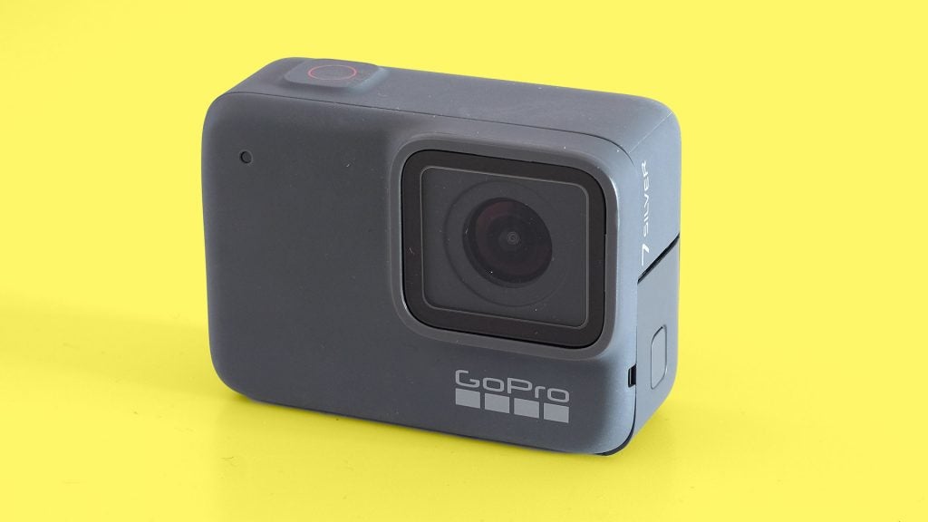Right angled view of a black GoPro Hero7 silver camera standing on a yellow background