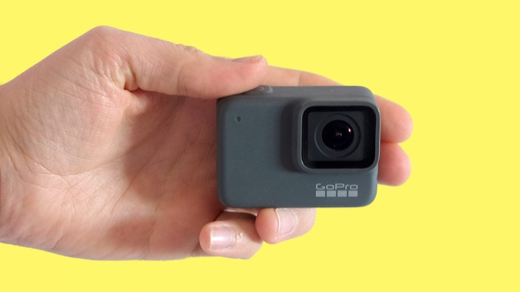 A black GoPro Hero7 silver camera held in hand on yellow background