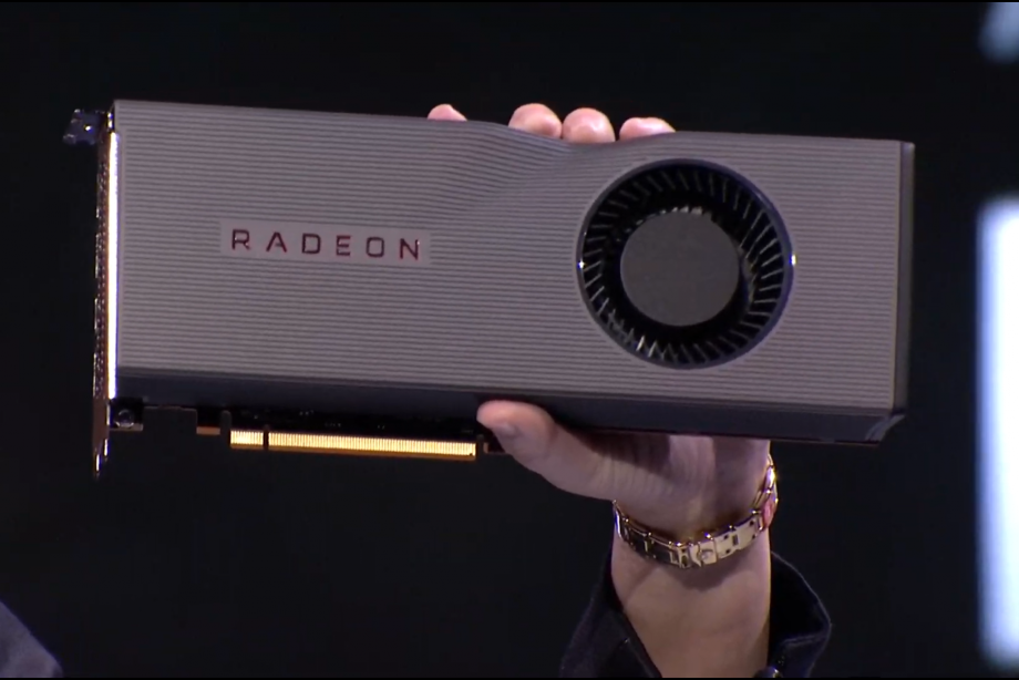A woman standing on stage with AMD Radeon 5700 XT displayed on screen behind