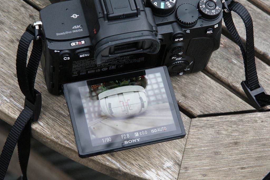 Back panel view of a black Sony A 7R standing on a wooden surface with back screen flipped horizontally to face up