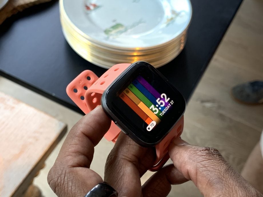 Top side view of a Fitbit Versa 2 wore on hand and it's side buttons being pressed