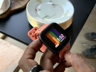 A Fitbit Versa 2 wore on hand displaying date and time with other details