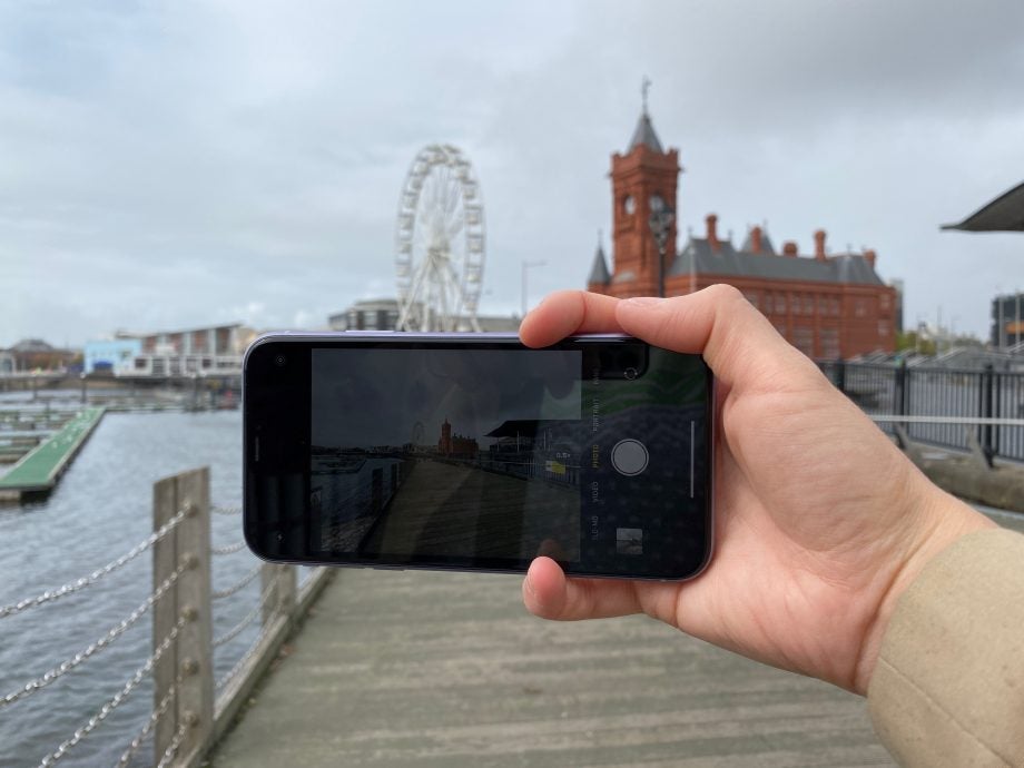An iPhone 11 held in hand displaying picture through camera, super wide angle