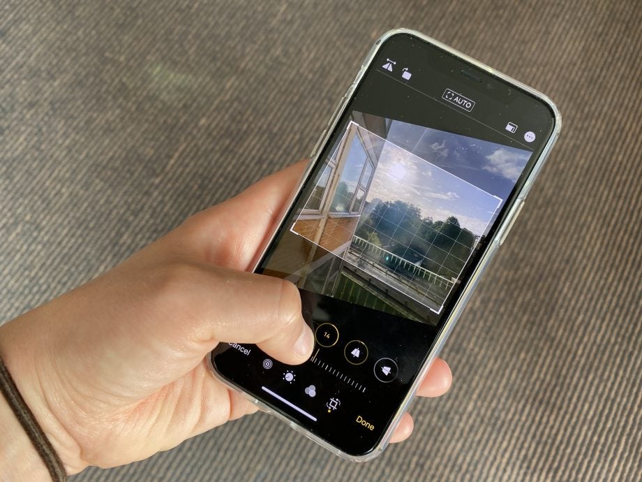 An iPhone 11 held in hand displaying an ongoing editing of a picture, adjust composition