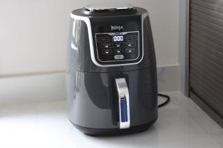 Left angled view of a Ninja Air Fryer Max AF160UK kept on a white table