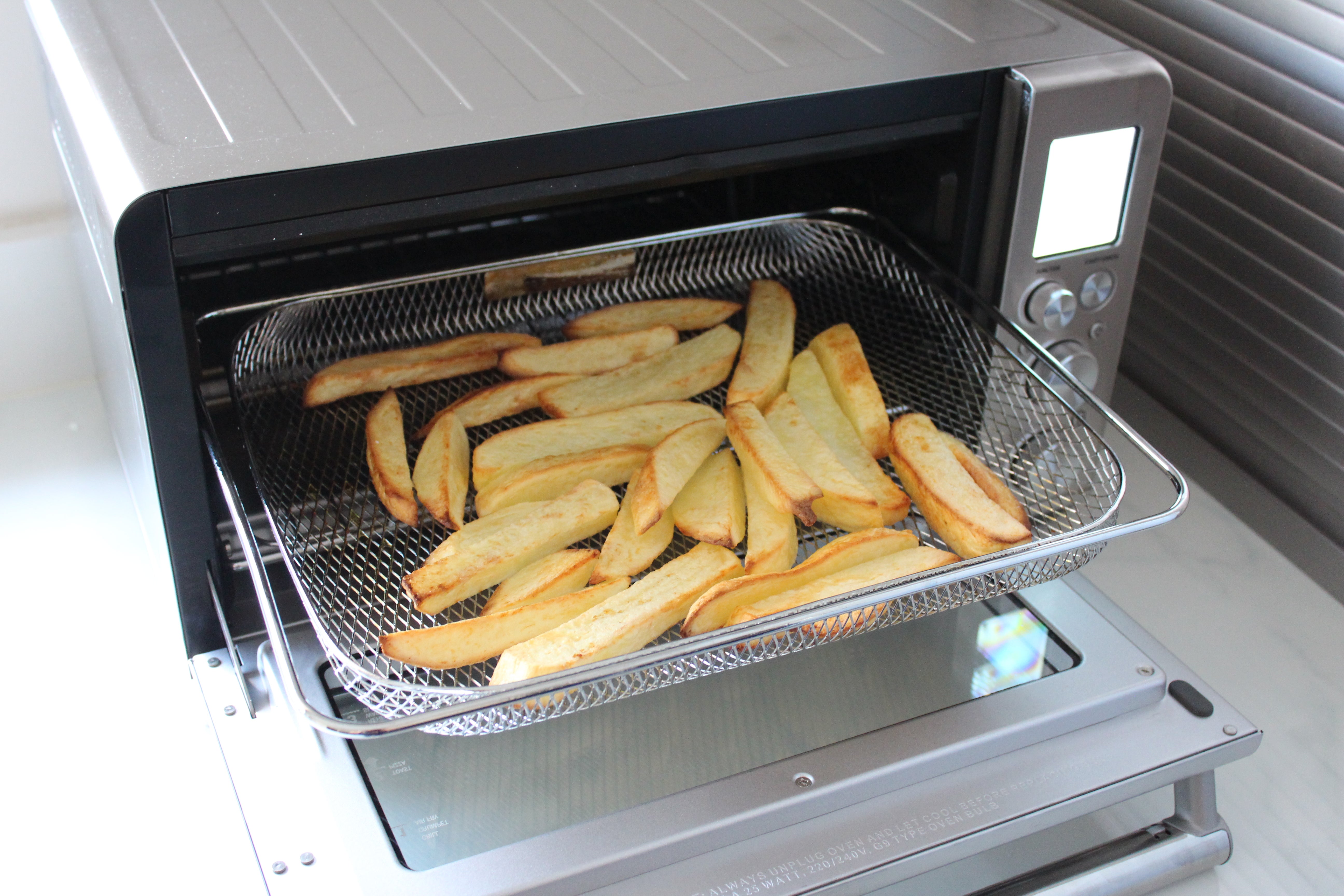Sage the Smart Oven Air Fry cooking chipsA silver Sage the Smart Oven Air Fry kept on a table with fried French fries kept on pulled out tray