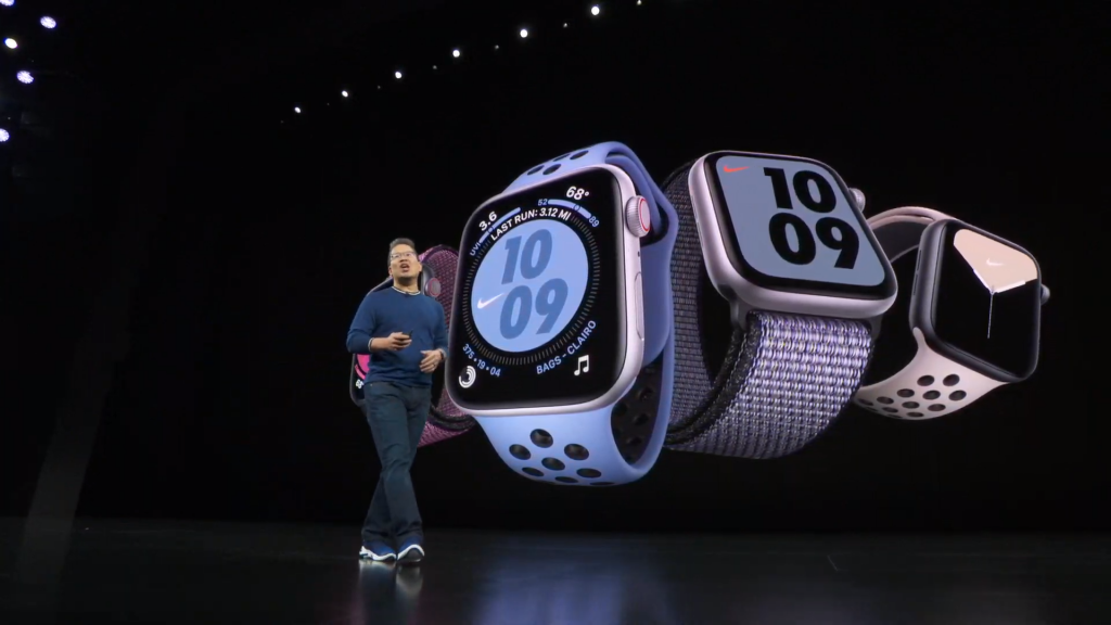 A man standing on stage with four different Apple Watch series 5 displayed on the screen behind