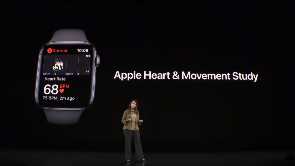 A woman standing on stage with Apple heart & movement study displayed on the screen behind