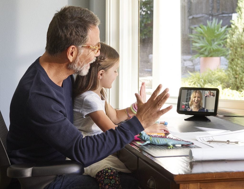 A father and a daughter sitting on a chair looking towards an Amazon Echo show 8 kept on the table