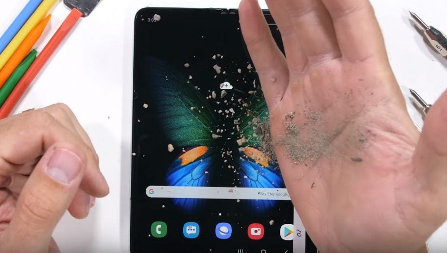 A wallpaper of Samsung Galaxy Fold's torture test, tiny stones being thrown on a Samsung Galaxy Fold kept on a white table