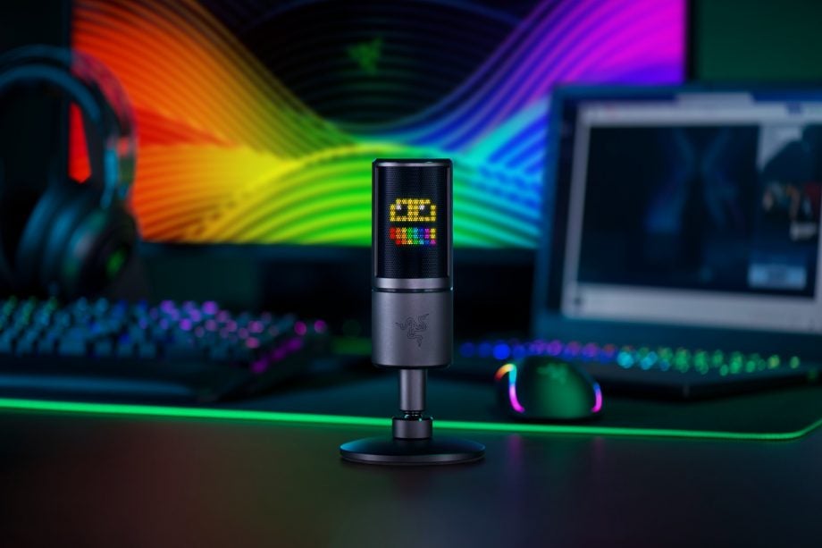 A silver Razer Seiren Emote mic standing on a table with streaming setup behind