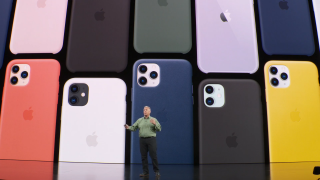 An old man standing on stage with an iPhone 11 color variants displayed on screen behind