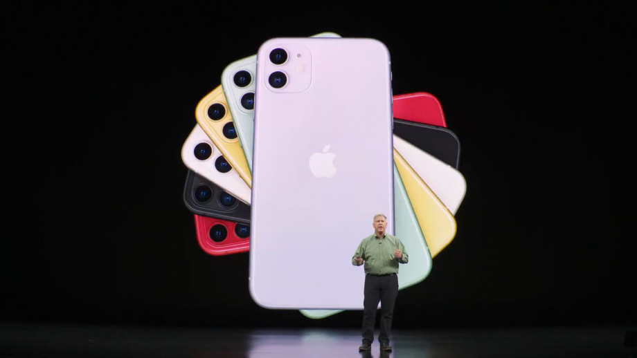 An old man standing on stage with iPhone 11 color variants displayed on screen behind