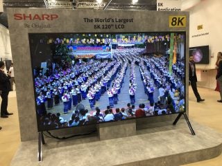 Left angled view of a black Sharp 120-in 8K TV standing on it's stand in a store
