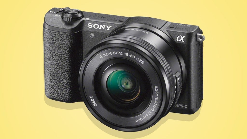 Right angled view of a black Sony Alpha 5100 camera standing on a yellow background