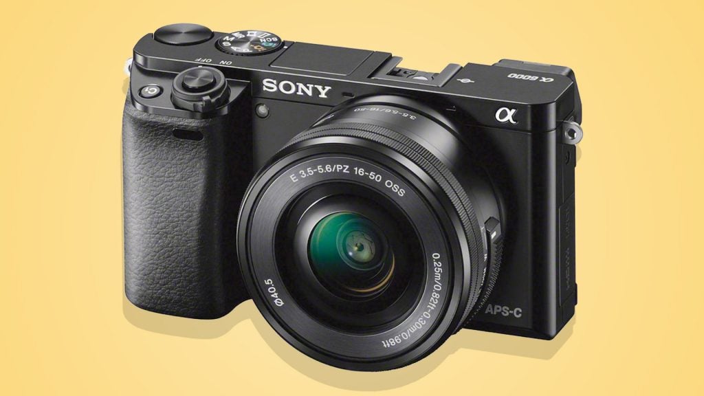 Right angled view of a black Sony Alpha 6000 camera standing on a yellow background
