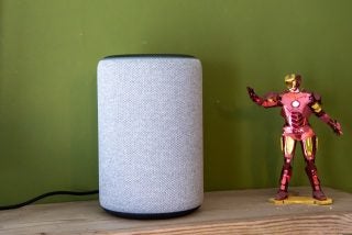 A white Amazon Echo 3rd Gen standing on a table beside Iron Man toy