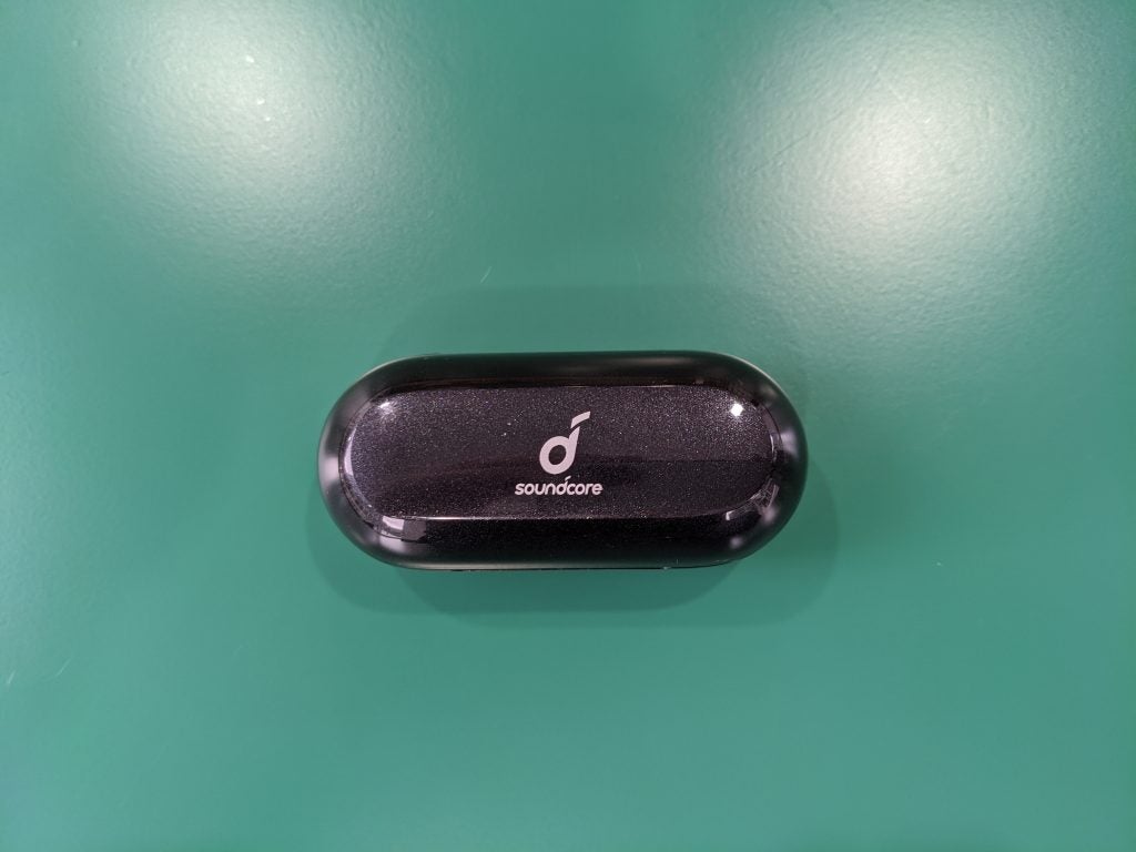 View from top of black Anker Soundcore Liberty Neo earbud's case kept on a green table