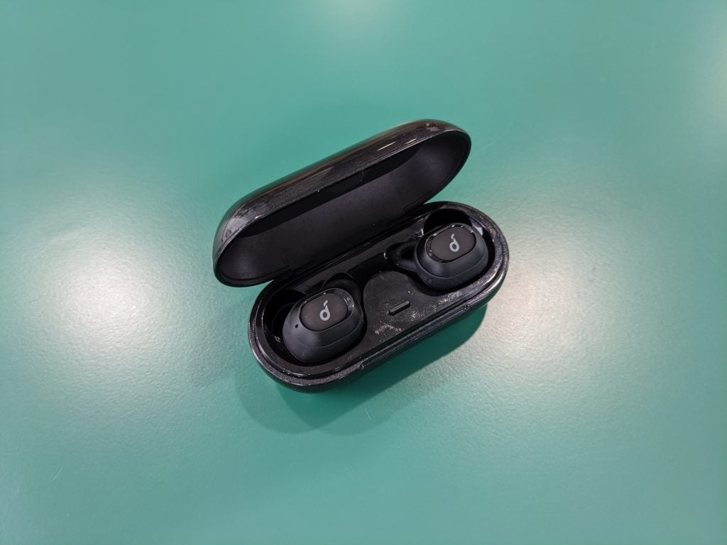 View from top of black Anker Soundcore Liberty Neo earbuds resting in it's case on a green table