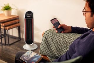 A white-black Dimplex MaxAir standing in a living room with a man sitting on couch using phone