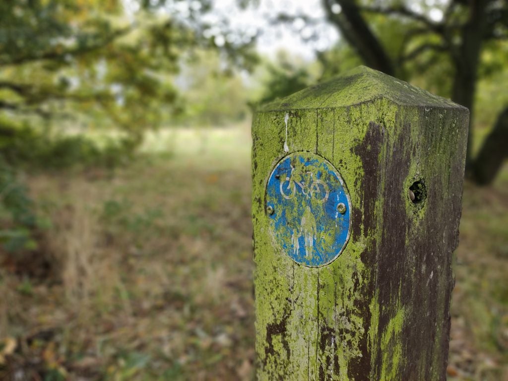 A wooden piece of block in an open field with a cycling and walking with children sign on it