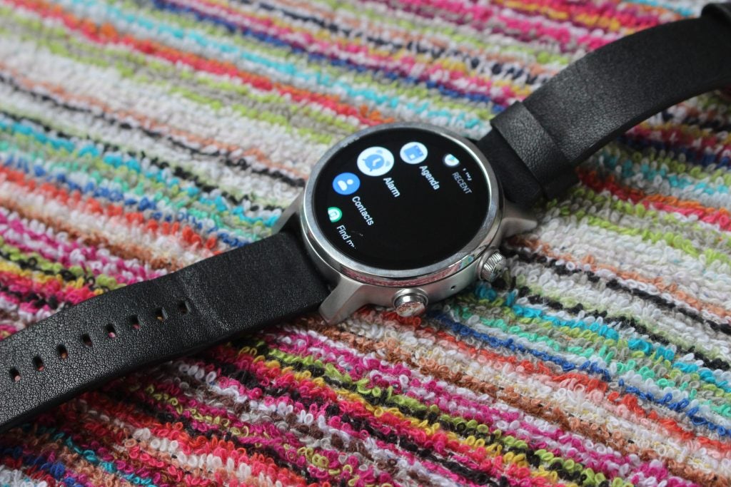 Smartwatch Motorola perak-hitam diletakkan di layar menu yang menampilkan karpet