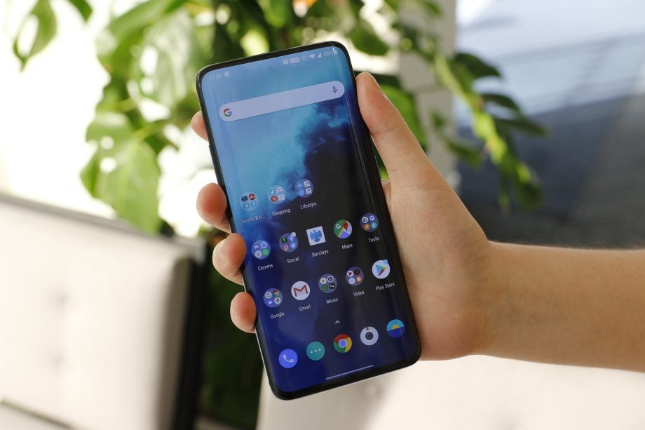 A One Plus 7T Pro held in hand displaying home screen