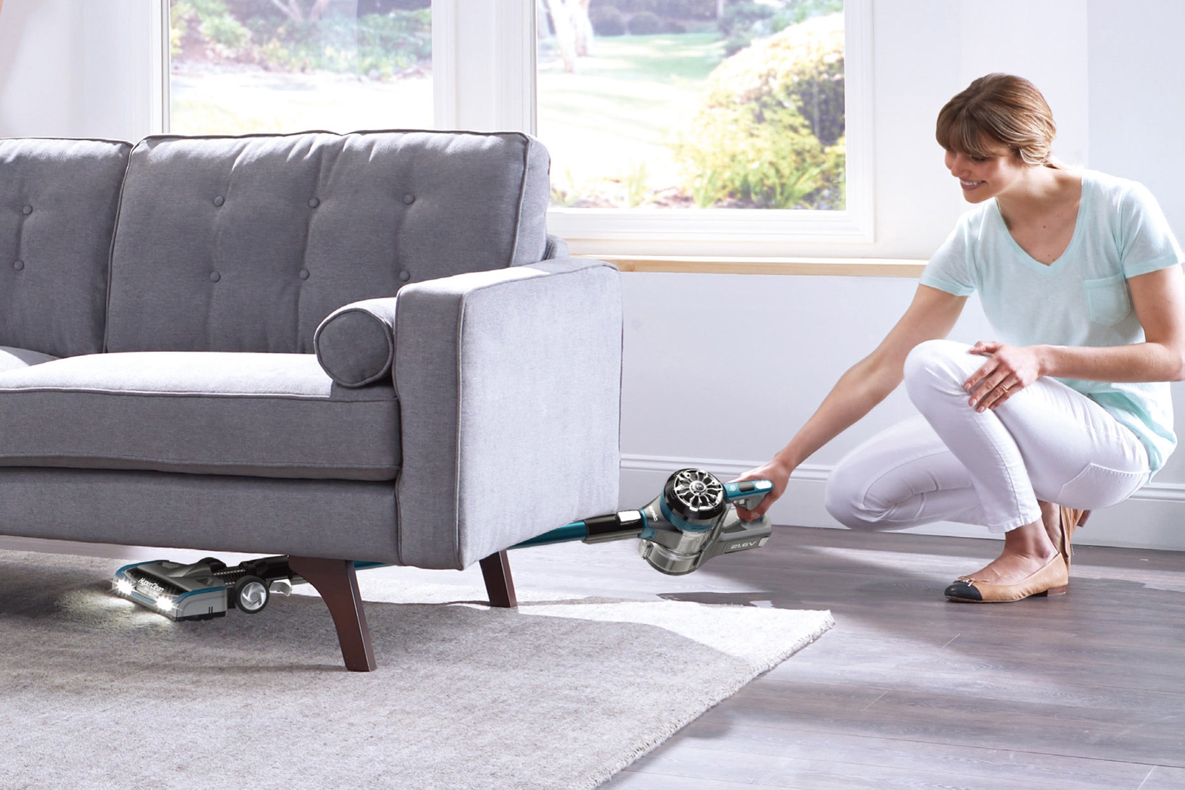 A Swan Hyperclean Eureka with vacuum cleaner held being used under a sofa on a carpet