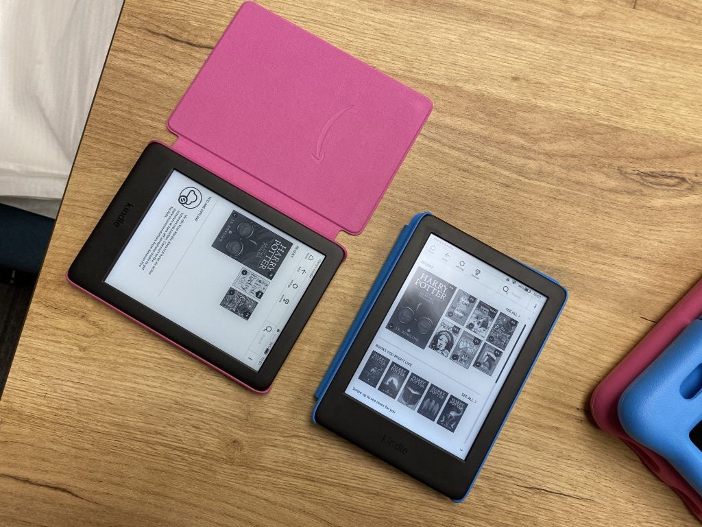 View from top of a blue and a pink Amazon Fire Kindle kept on a wooden table displaying books to read