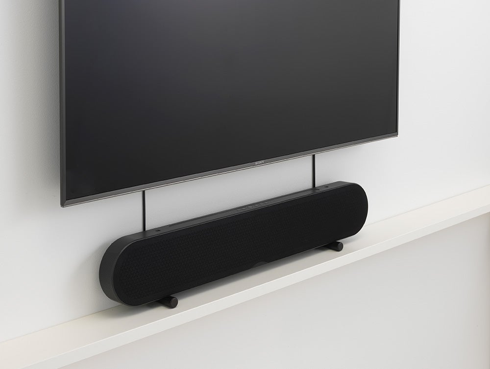 DALI Katch OneA black Dali Katch One soundbar kept on a table below a TV mounted on wall