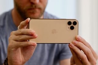 Back panel view of a cream colored iPhone 11 Pro held in hand horizontally facing back