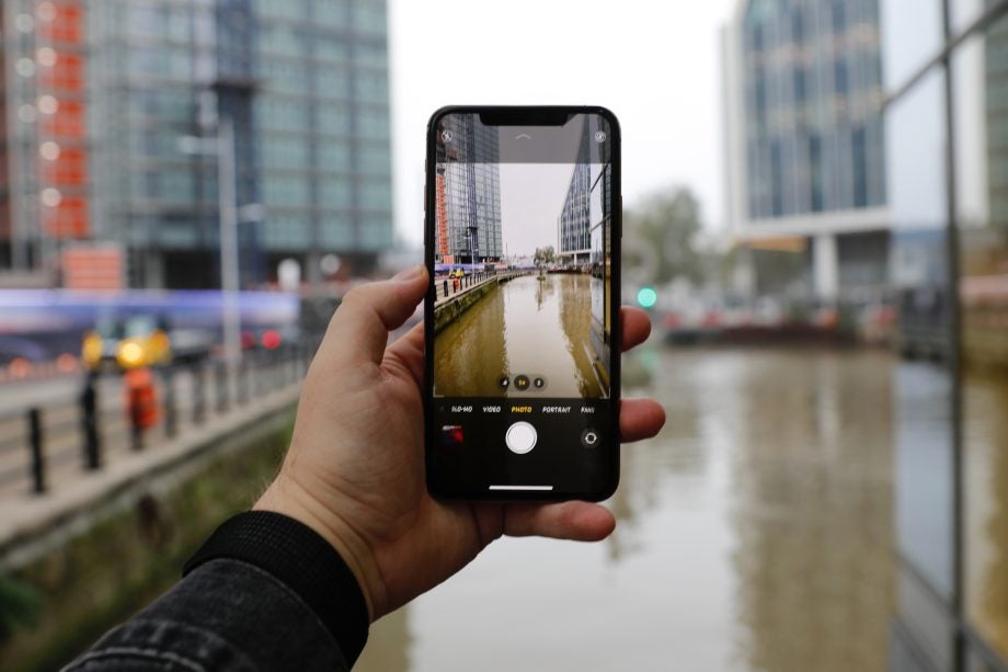 An iPhone 11 Pro Max held in hand displaying picture of a lake via camera