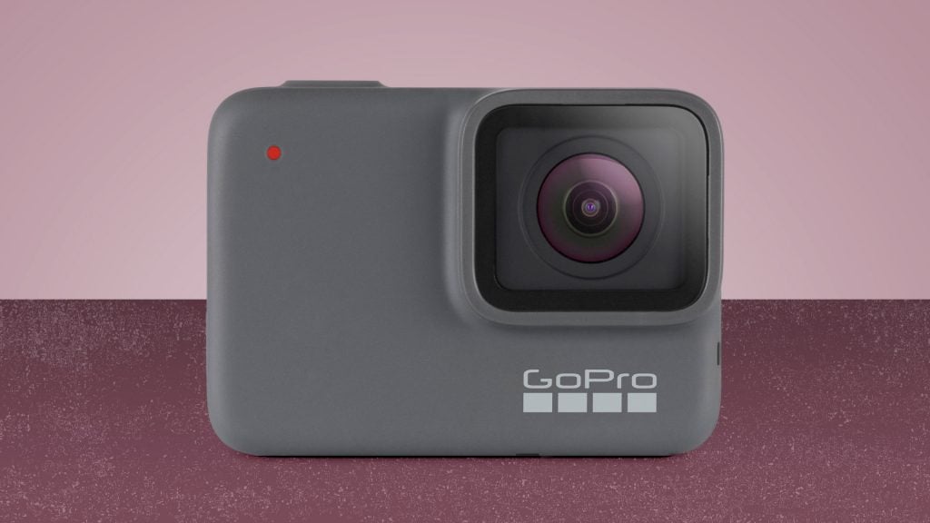 A silver GoPro Hero 8 camera standing on light magenta background