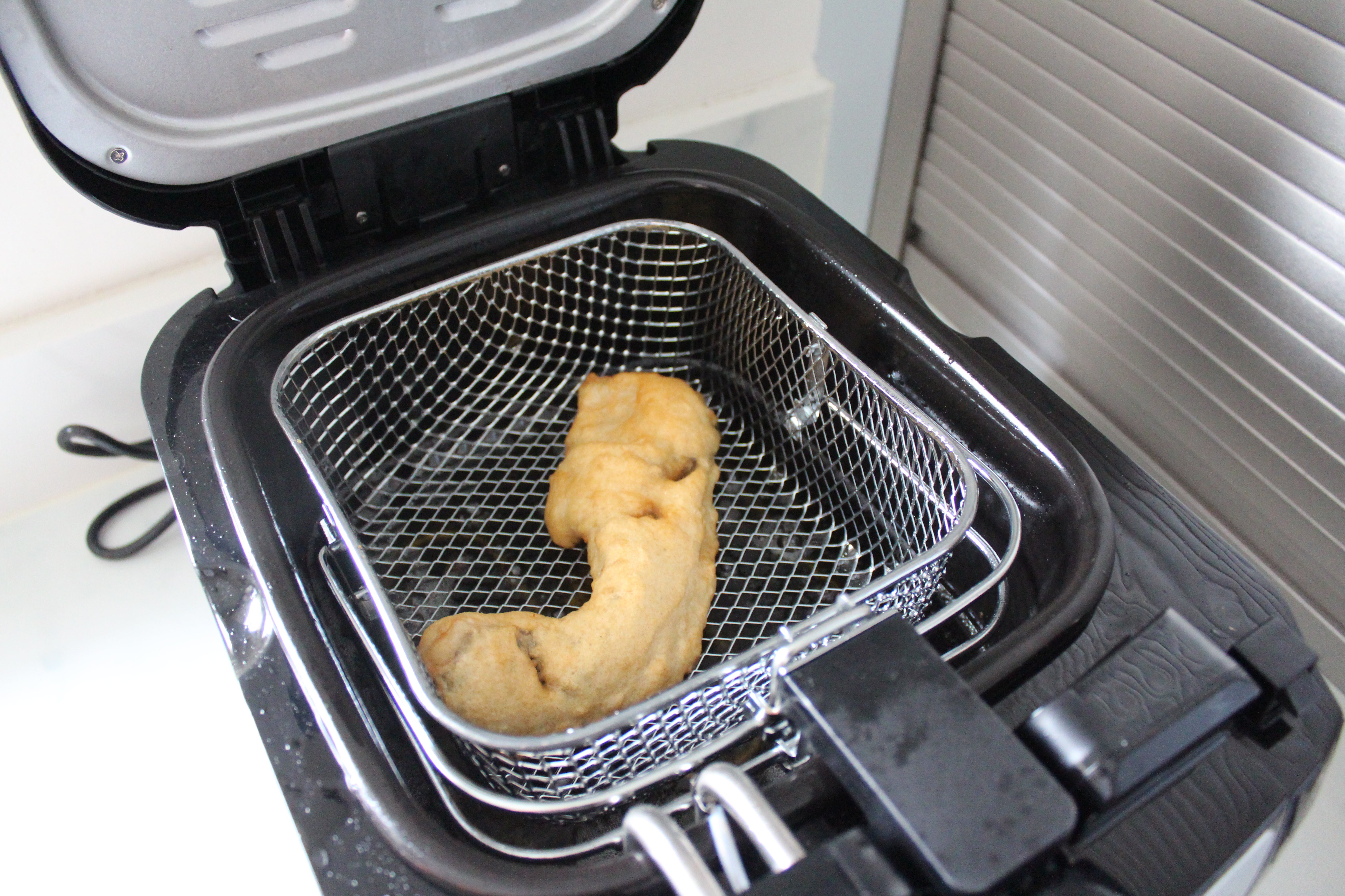 Russell Hobbs Digital Deep Fryer 24580 fishA black Rusell Hobbs Digital deep fryer kept on a kitchen platform with a fried bite kept inside itA black Rusell Hobbs Digital deep fryer kept on a kitchen platform with brown round quick bites being fried inside