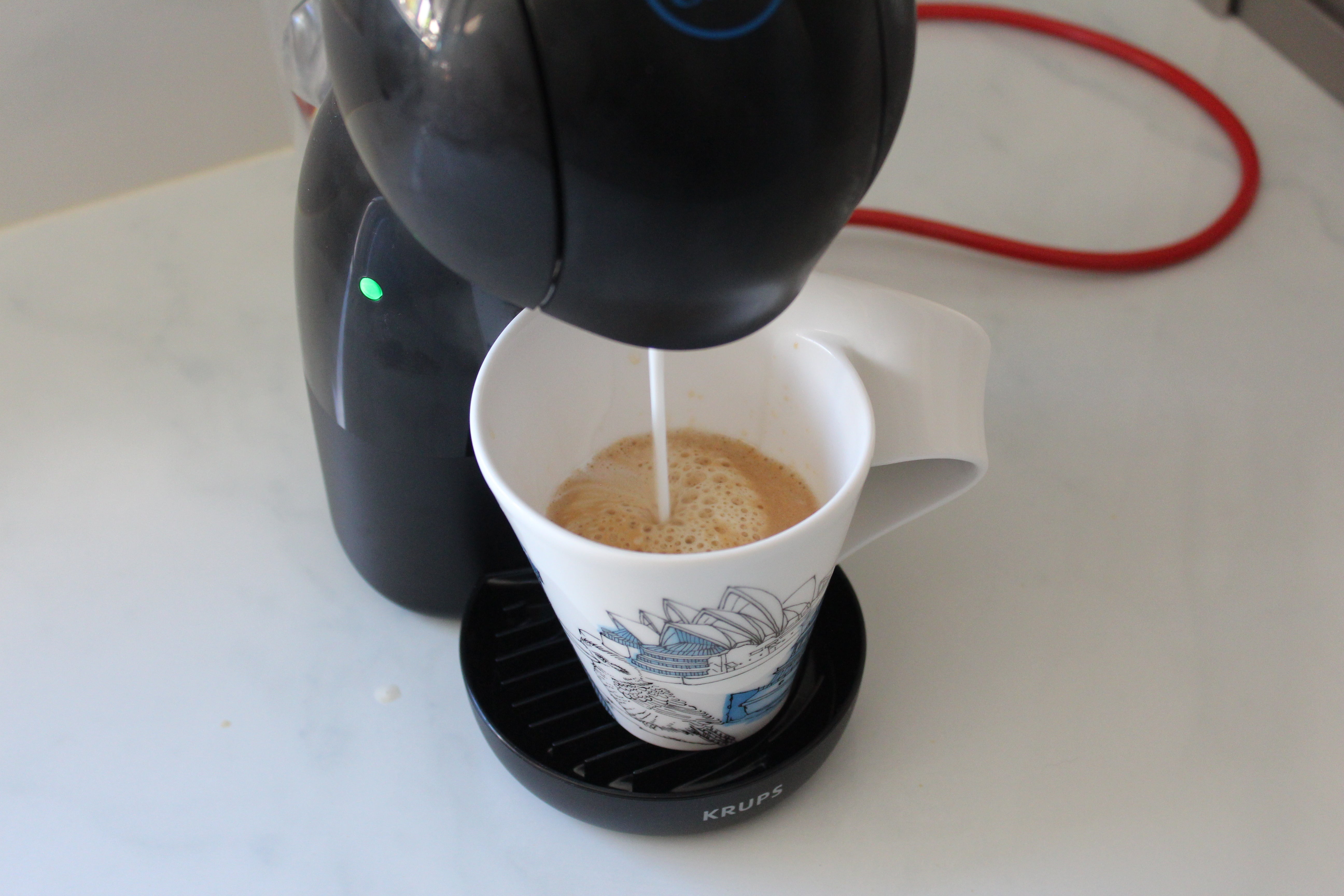 Nescafé Dolce Gusto Piccolo XS milkA coffee mug being filled from Nescafe Dolce Gusto Piccolo XS standing on a table