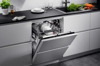 A silver-black AEG dishwasher fixed in a kitchen, half opened front panel, utensils placed inside