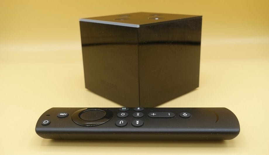 A black Amazon Fire TV Cube with it's black remote on front kept on a yellow background