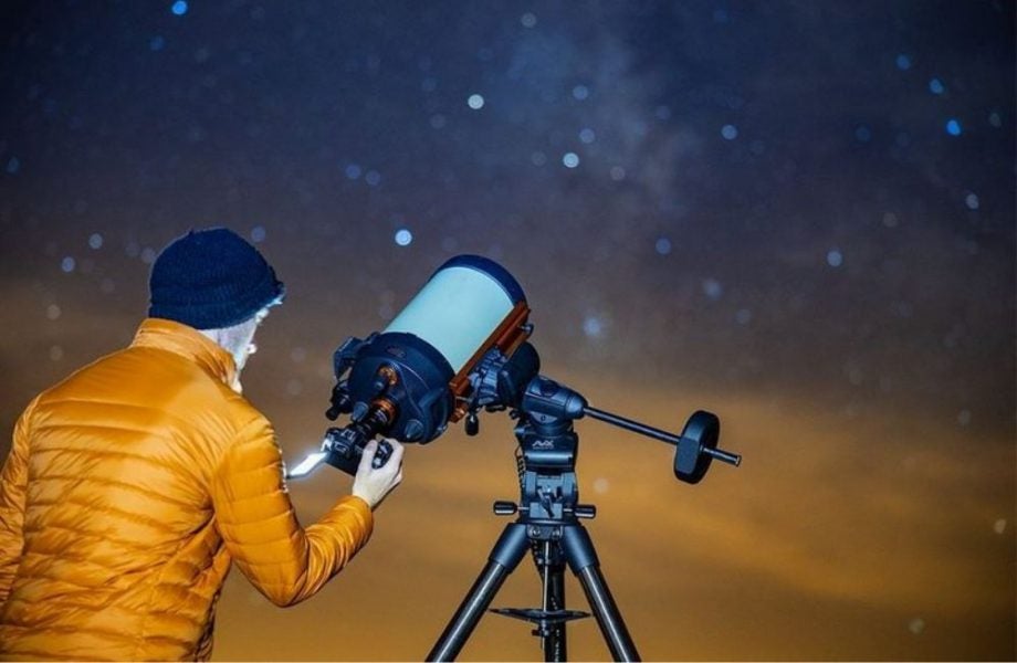 A wallpaper of Canon EOS RA camera, a man standing beside it and pointing it towards the night sky