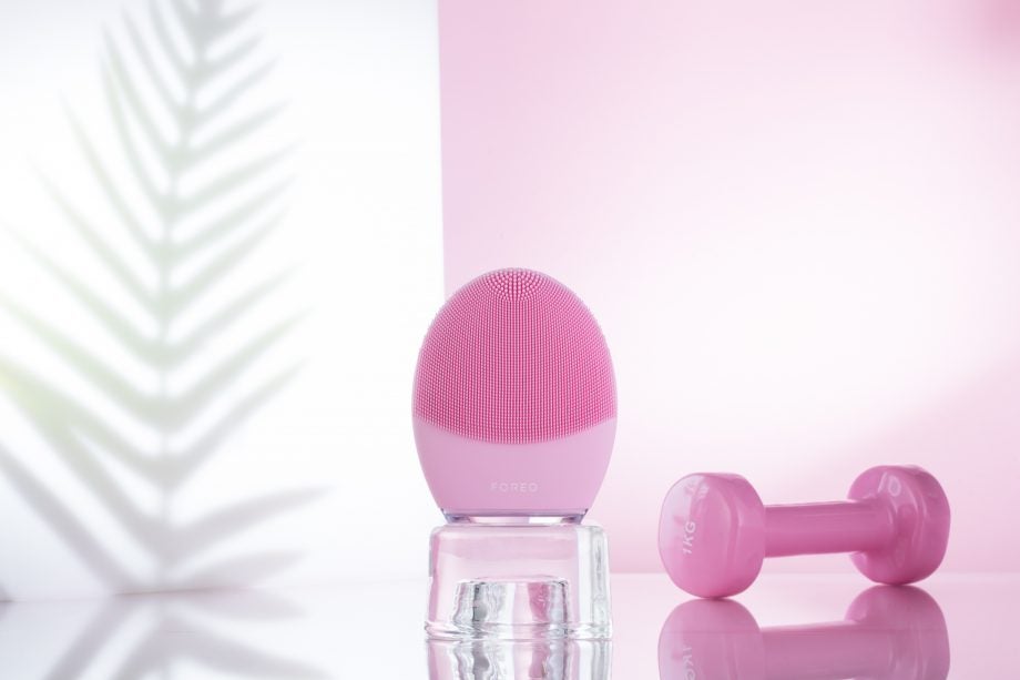 A pink Foreo Luna 3 sonic cleansing brush kept on a table beside a tiny 1Kg pink dumble