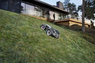 A gray Husqvarna Automover 435X AWD moving down on a slope in a lawn