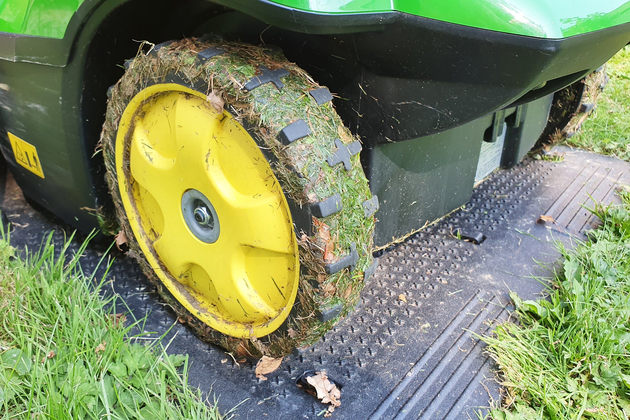 Close up view of dirty tyres of John Deere Tango robot lawnmower resting on it's station in a lawn