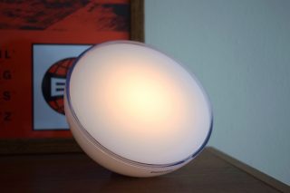 Left angled view of a Philips Hue Go smart light standing on a table, turned on