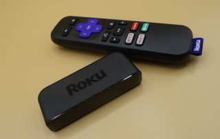 A black Roku Premiere box kept beside it's black remote on a table