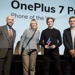 A man and a woman receiving award from two men on stage, One Plus 7 Pro displayed on screen behind, Trusted Reviews Awards