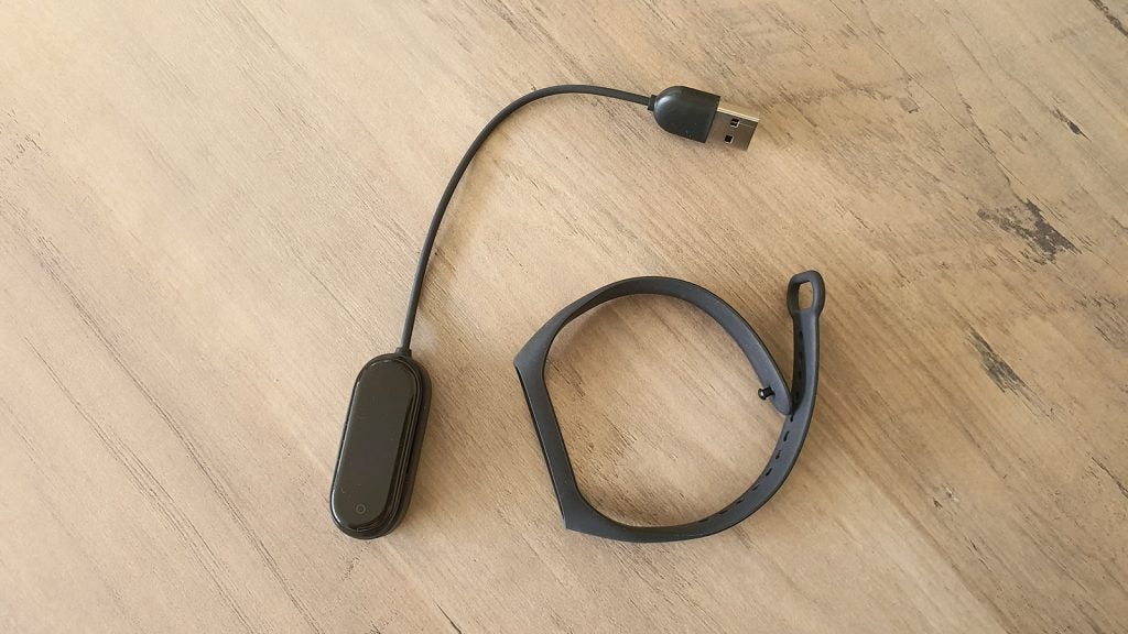 View from top of a disassembled Xiaomi Mi Band 4 kept on a table with a charging cable connected to screen