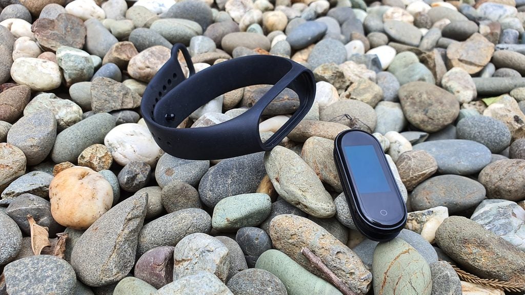A gray-black Xiaomi Mi Band 4 tied on a stemA gray-black Xiaomi Mi Band 4 disassembled kept on pebbles, small screen removed from band
